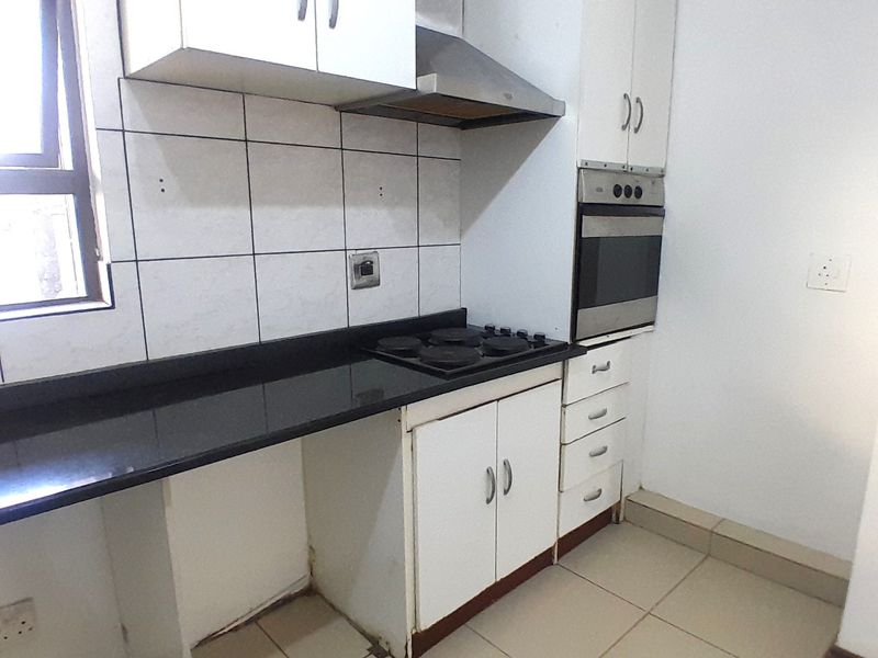 Compact kitchen featuring white cabinetry, black granite countertops, built-in oven, and hob, with tiled flooring and splashback.