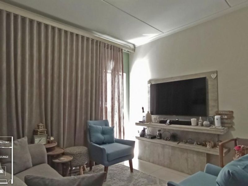 A comfortable living room featuring a built-in media console, tiled flooring, and floor-to-ceiling curtains providing access to the balcony.