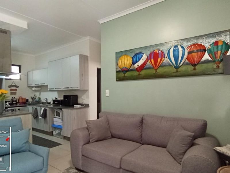 Open-plan living area featuring a functional kitchen with built-in cabinetry, stainless steel extractor fan, and tiled flooring, seamlessly connected to the lounge space.