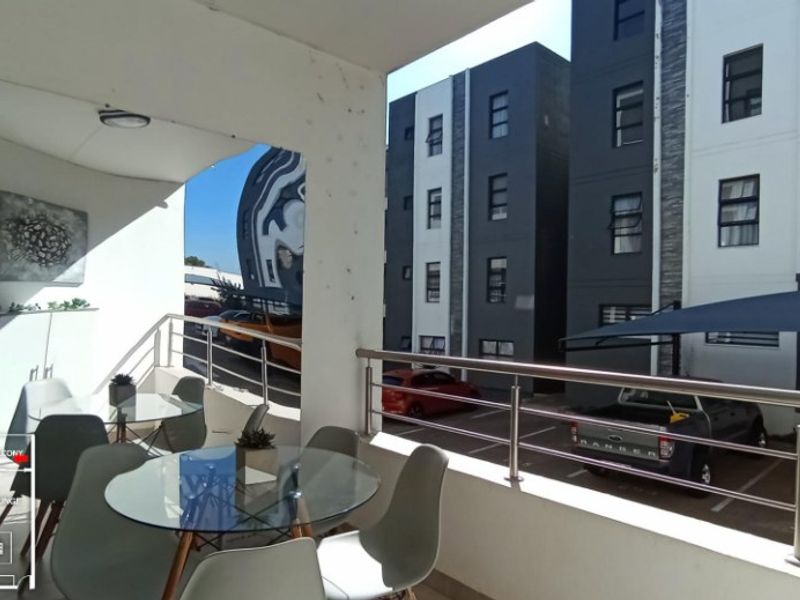A covered balcony featuring a stainless steel balustrade, overlooking the apartment complex parking area.