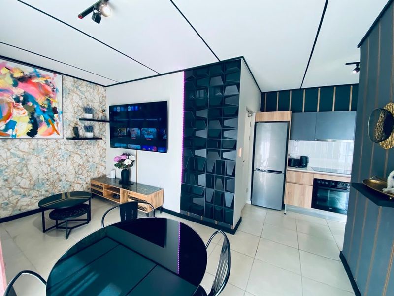 Modern open-plan living area featuring a contemporary kitchen with built-in appliances, stylish wall treatments, and sleek tiled flooring throughout.