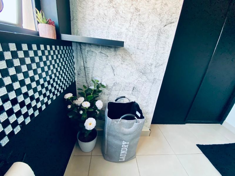 A small laundry area featuring tiled flooring, a floating shelf, and a textured feature wall with a black and white checkered accent.