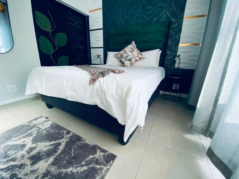 A well-maintained bedroom featuring tiled flooring and decorative accent wall paneling behind the bed area.