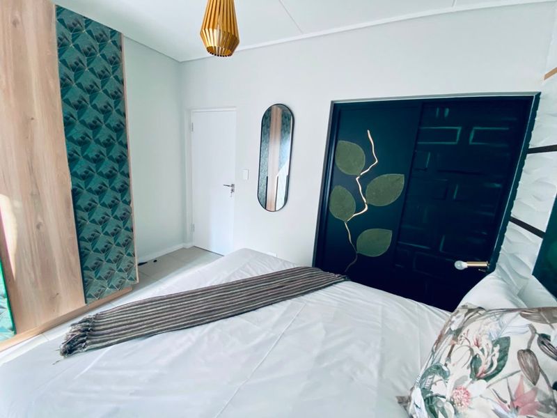 A well-maintained bedroom featuring a built-in wardrobe with decorative paneling and a modern pendant light fixture.