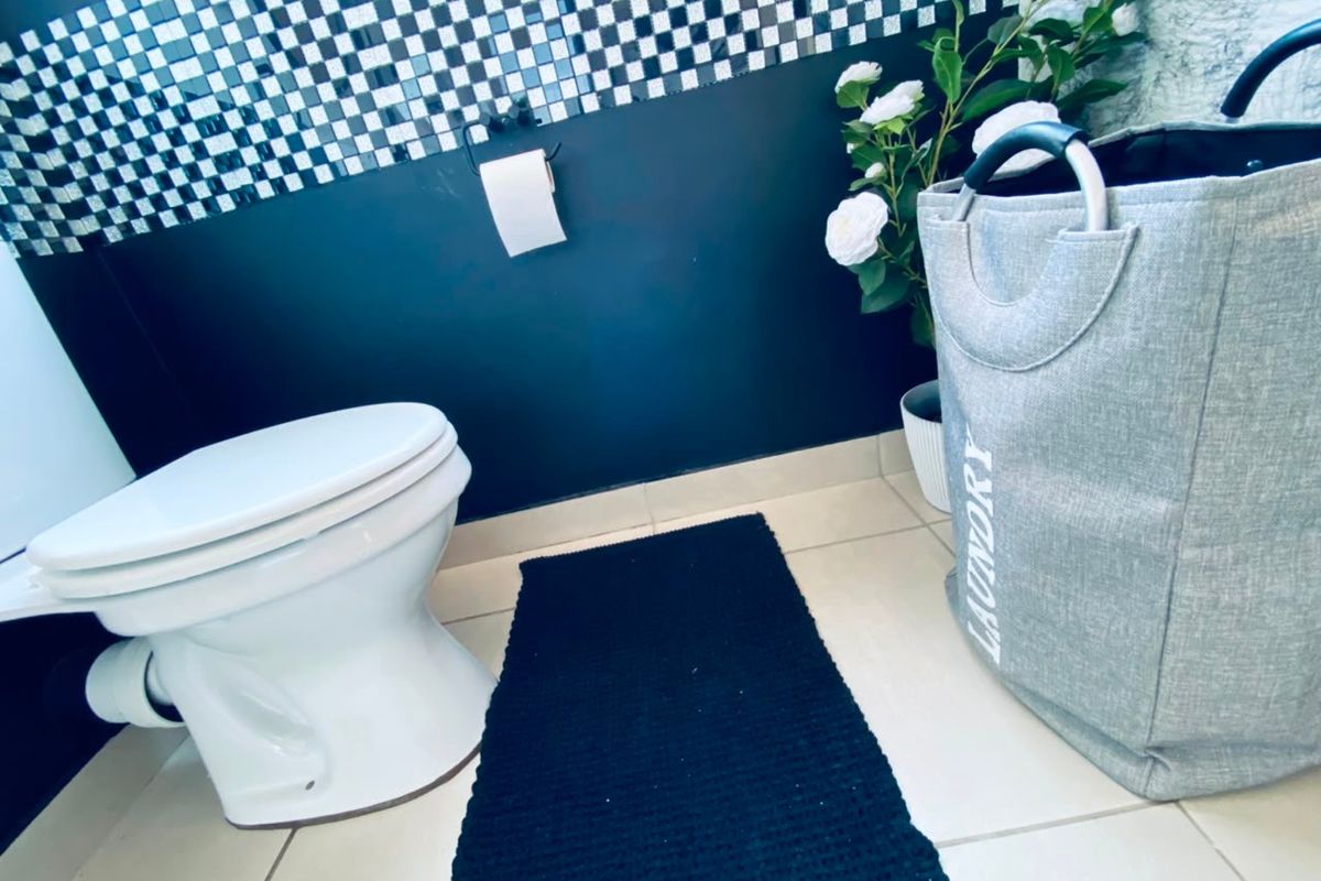 A bathroom featuring a white toilet, tiled flooring, and a decorative black and white mosaic wall accent.