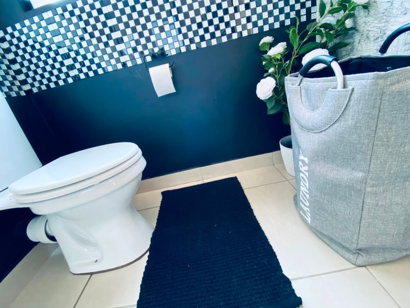 A bathroom featuring a white toilet, tiled flooring, and a decorative black and white mosaic wall accent.