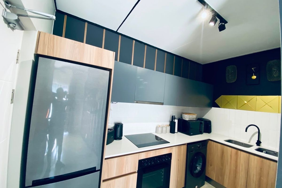Modern kitchen featuring wood-tone and grey cabinetry, sleek white countertops, built-in oven, electric hob, and contemporary track lighting.
