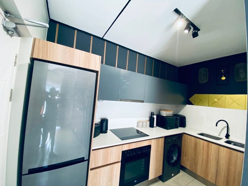 Modern kitchen featuring wood-tone and grey cabinetry, sleek white countertops, built-in oven, electric hob, and contemporary track lighting.
