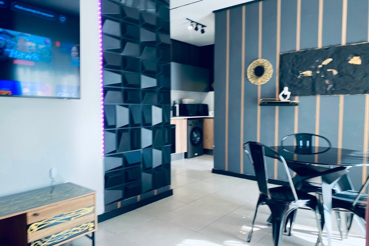Modern open-plan living and dining area featuring contemporary wall paneling, tiled floors, and a compact kitchen with integrated laundry appliances.