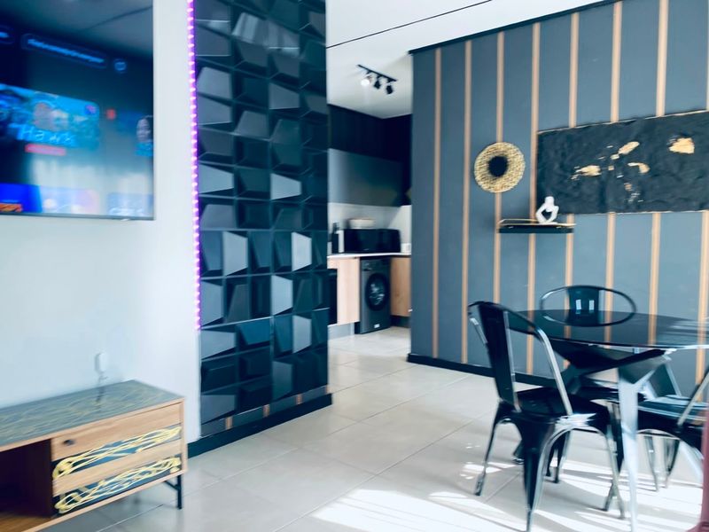 Modern open-plan living and dining area featuring contemporary wall paneling, tiled floors, and a compact kitchen with integrated laundry appliances.
