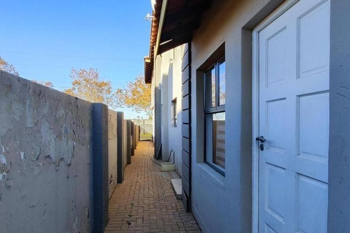 A narrow side passage featuring a paved walkway, external access door, and a boundary wall showing signs of weathered paint and surface deterioration.