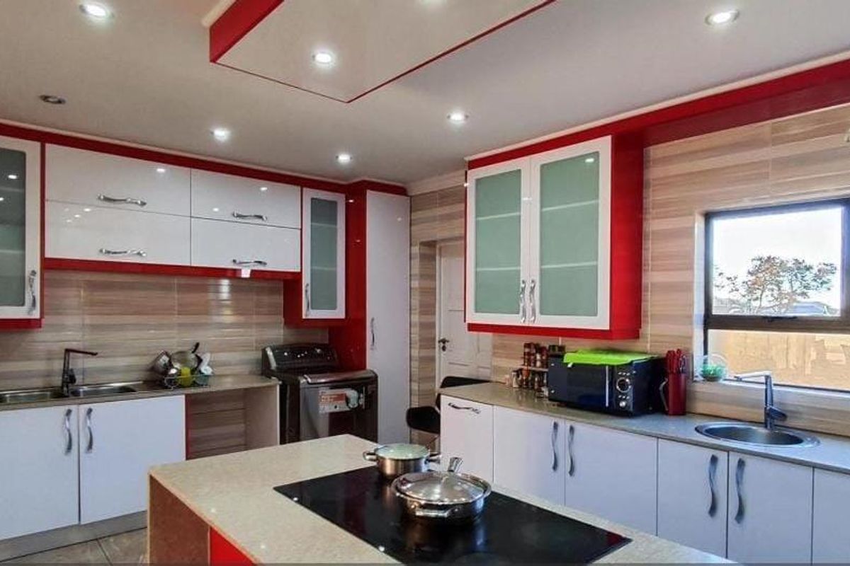 Modern kitchen featuring high-gloss white and red cabinetry, a central island with an integrated hob, and tiled splashbacks with ample natural light.
