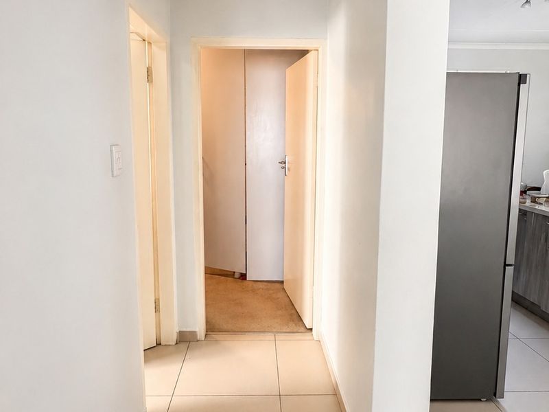 A clean, neutral hallway featuring tiled flooring and access to adjacent rooms, providing a bright and functional transition space within the apartment.