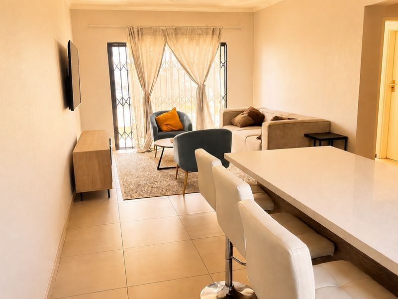 An open-plan living and dining area featuring tiled flooring, a breakfast bar, and a sliding door with a security gate leading to the exterior.