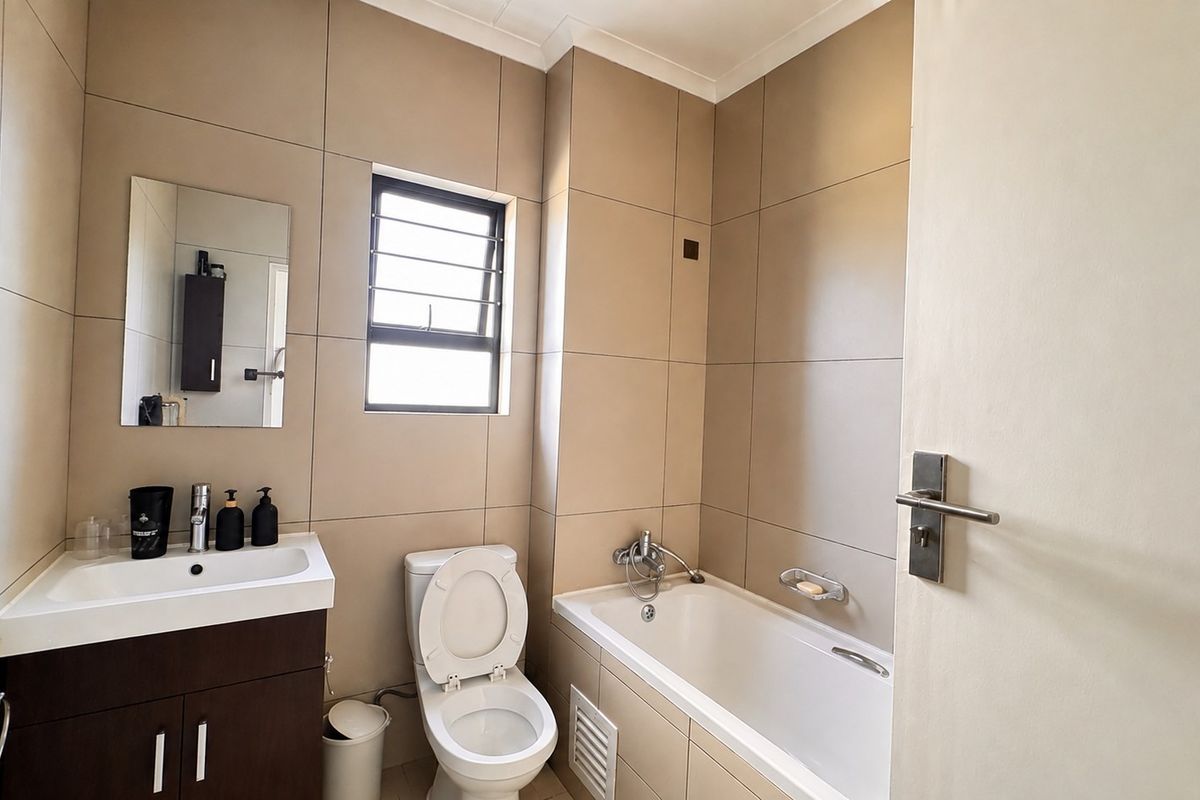 A functional bathroom featuring a vanity cabinet, basin, toilet, and a bathtub with tiled walls and flooring.