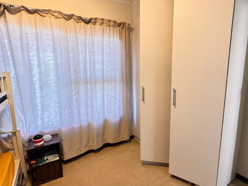 A bedroom featuring neutral carpeted flooring and white built-in cupboards, providing functional storage space.