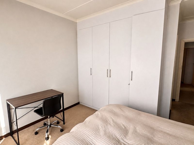 A functional bedroom featuring built-in cupboards, neutral wall finishes, and carpeted flooring, providing a clean and practical living space.