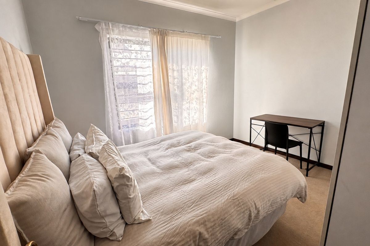 A functional bedroom featuring carpeted flooring, a built-in wardrobe, and natural light through a window with curtain fixtures.