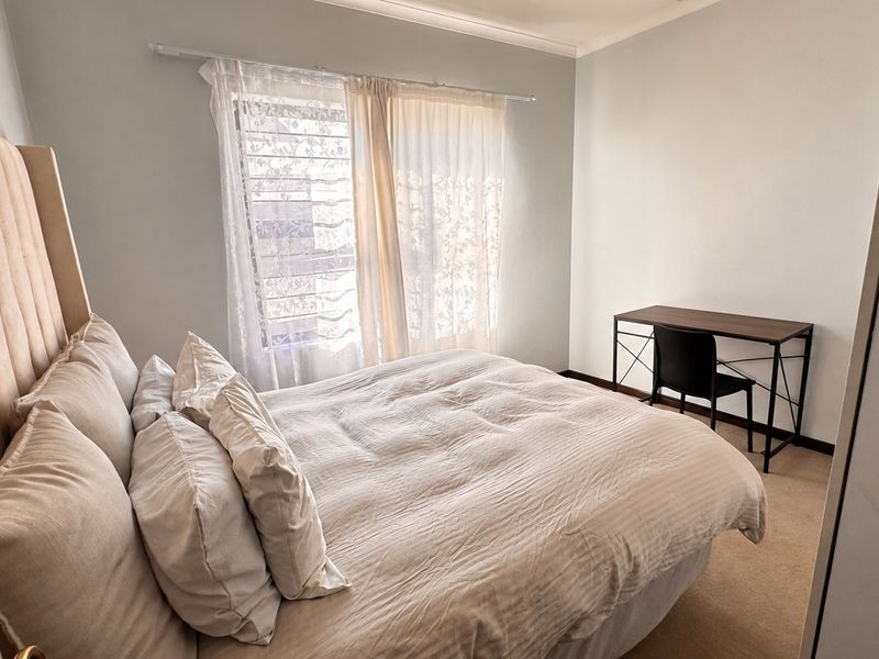 A functional bedroom featuring carpeted flooring, a built-in wardrobe, and natural light through a window with curtain fixtures.