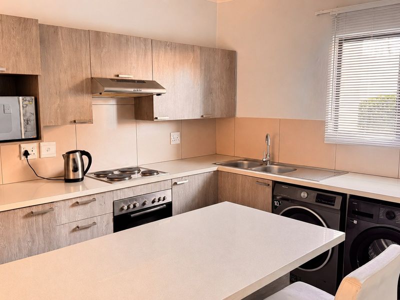 Modern kitchen featuring light wood-grain cabinetry, integrated appliances, ample countertop space, and a functional layout with a breakfast bar area.