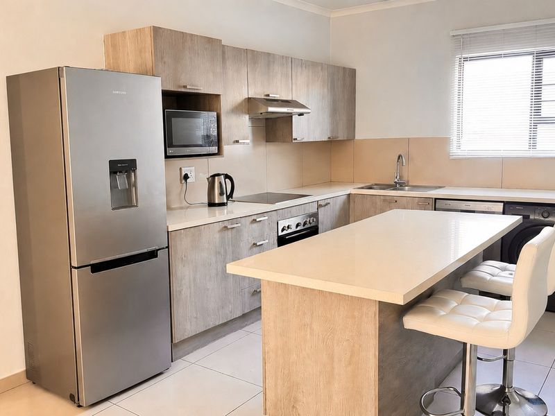 Modern kitchen featuring light wood-finish cabinetry, stone countertops, a central island, and integrated appliances, offering a clean and functional culinary space.