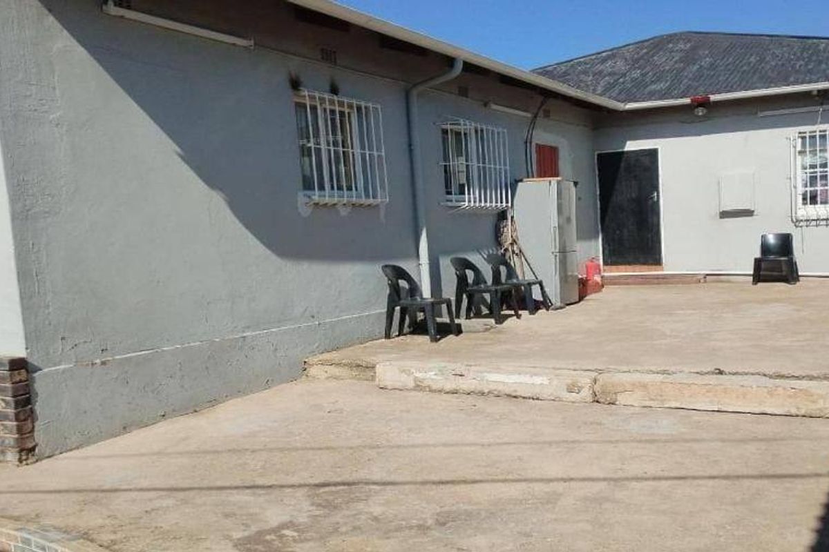 Rear exterior view featuring a concrete patio area, security-barred windows, and an external geyser unit, showing signs of wear and weathering.