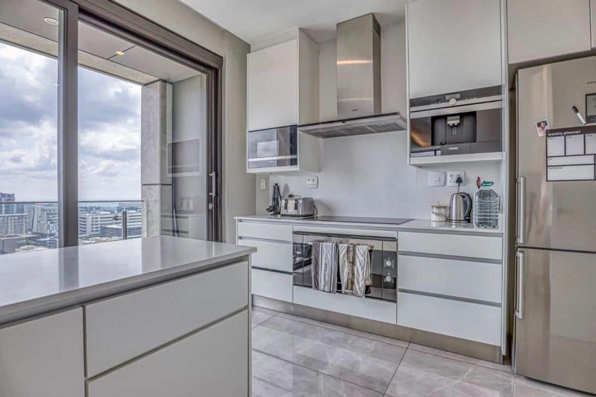 Modern kitchen featuring sleek white cabinetry, integrated appliances, stone countertops, and large format floor tiles, with direct access to a balcony.