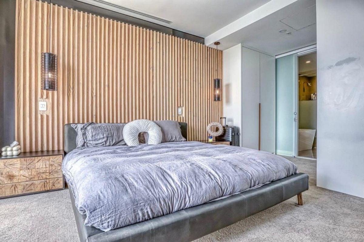 Modern bedroom featuring a stylish timber slat accent wall, built-in cabinetry, and an en-suite bathroom accessible via a sliding glass door.