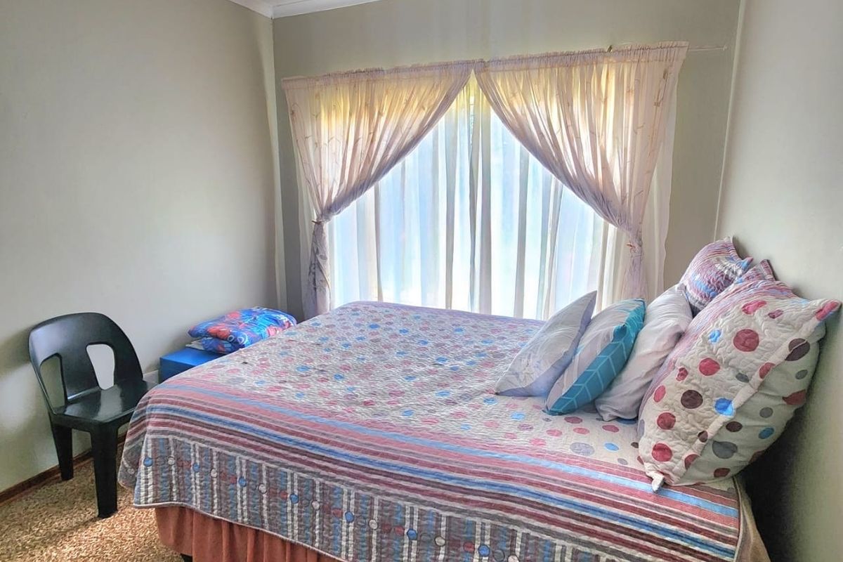 A standard bedroom featuring carpeted flooring, a ceiling fan, and large windows with curtain rails, offering a functional and neutral living space.