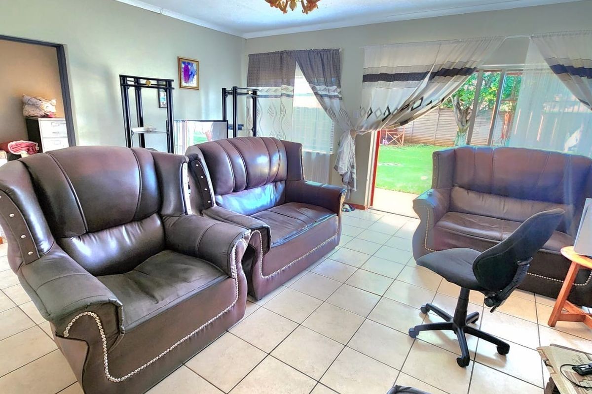 A living room featuring tiled flooring, a central ceiling light fixture, and a sliding glass door providing access to the rear garden.