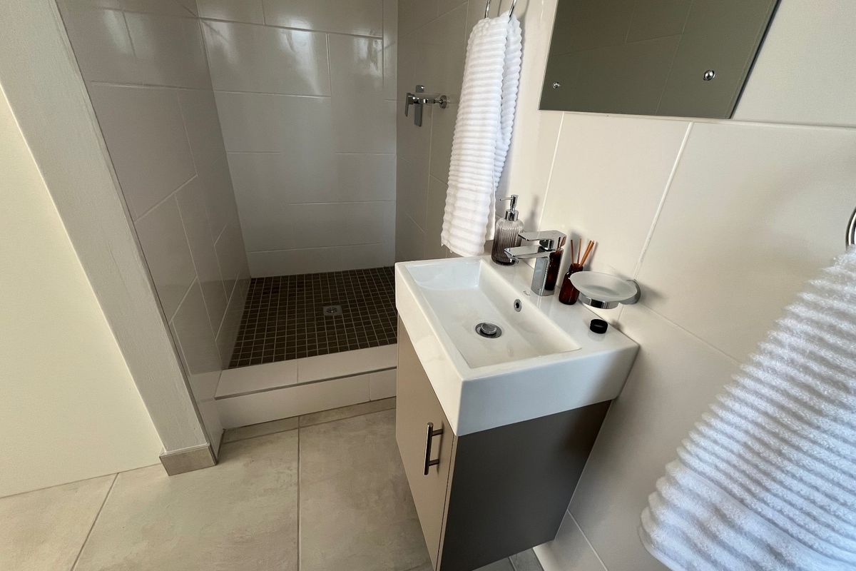A modern, compact bathroom featuring a wall-mounted vanity with a ceramic basin, chrome fixtures, and a tiled walk-in shower area.