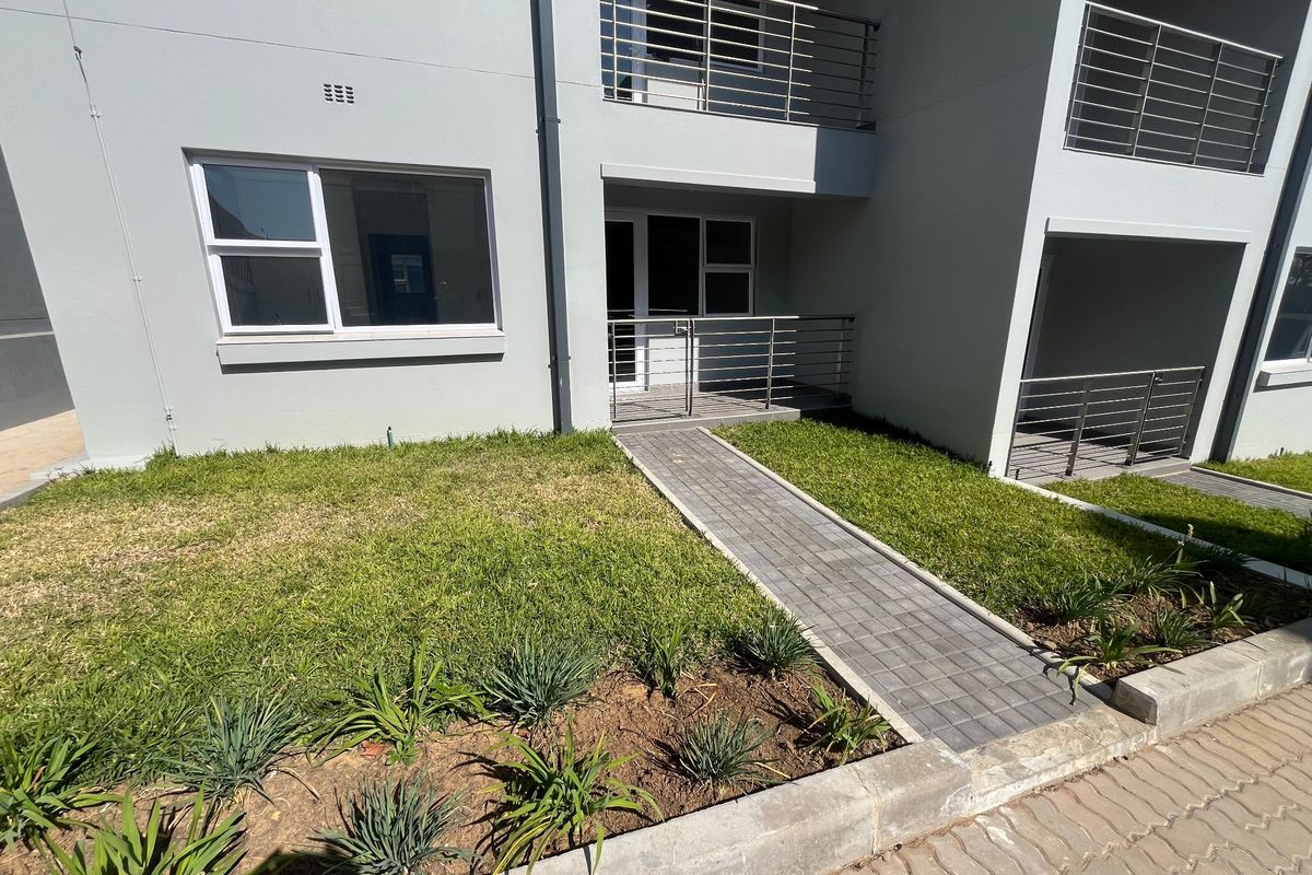 Ground floor apartment exterior featuring a paved walkway, landscaped garden beds, and modern stainless steel balcony railings.