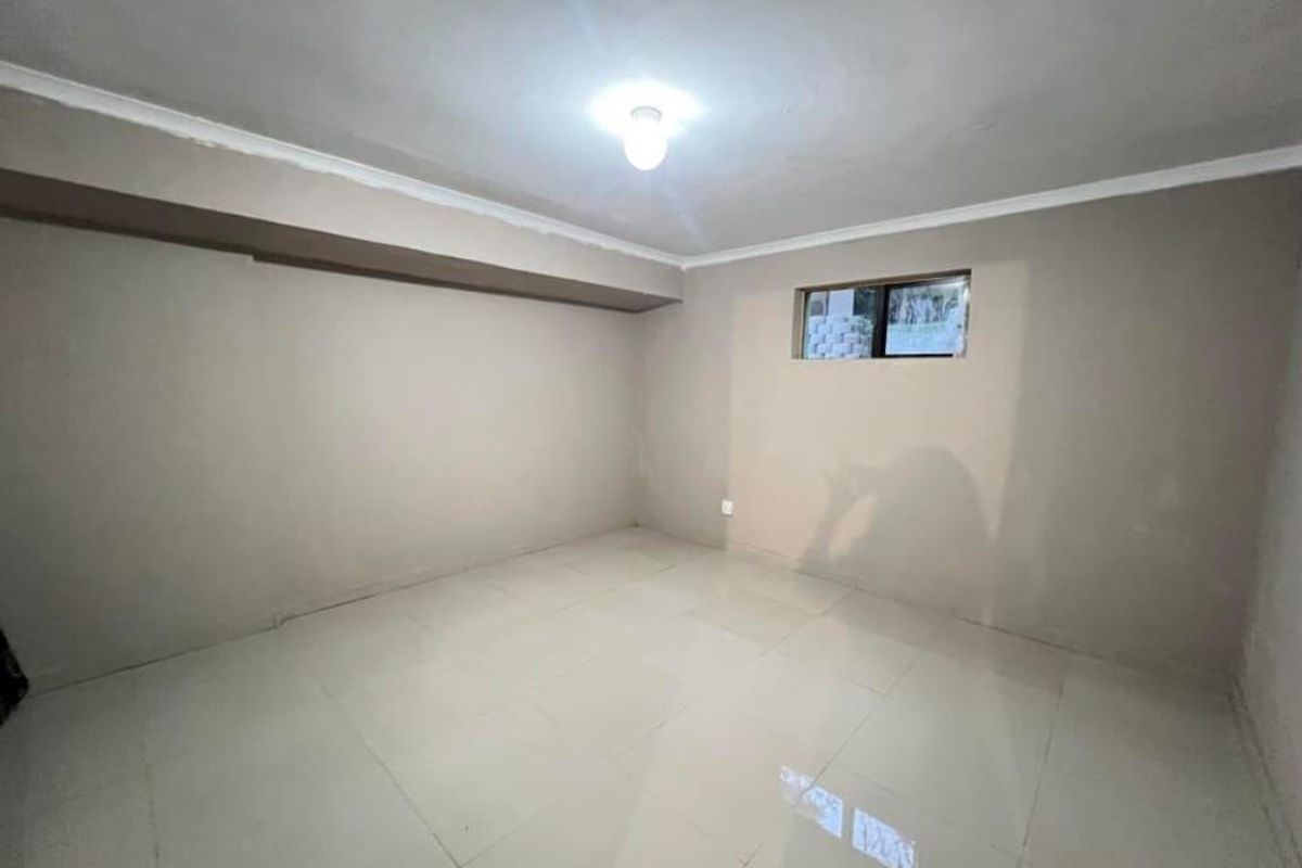 An empty, neutral-toned bedroom featuring tiled flooring, a small high-level window, and simple cove cornicing, ready for personalization.