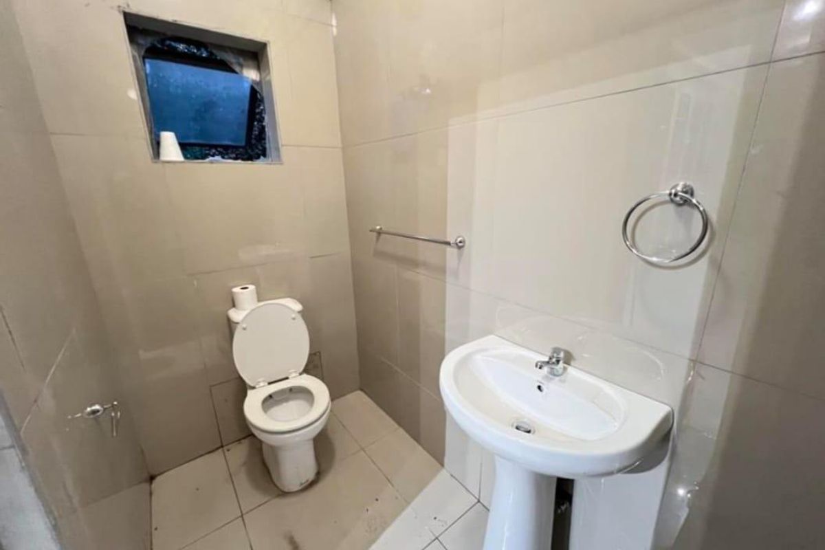 A compact bathroom featuring a pedestal washbasin, toilet, and tiled finishes. The space requires maintenance, specifically regarding the damaged window.