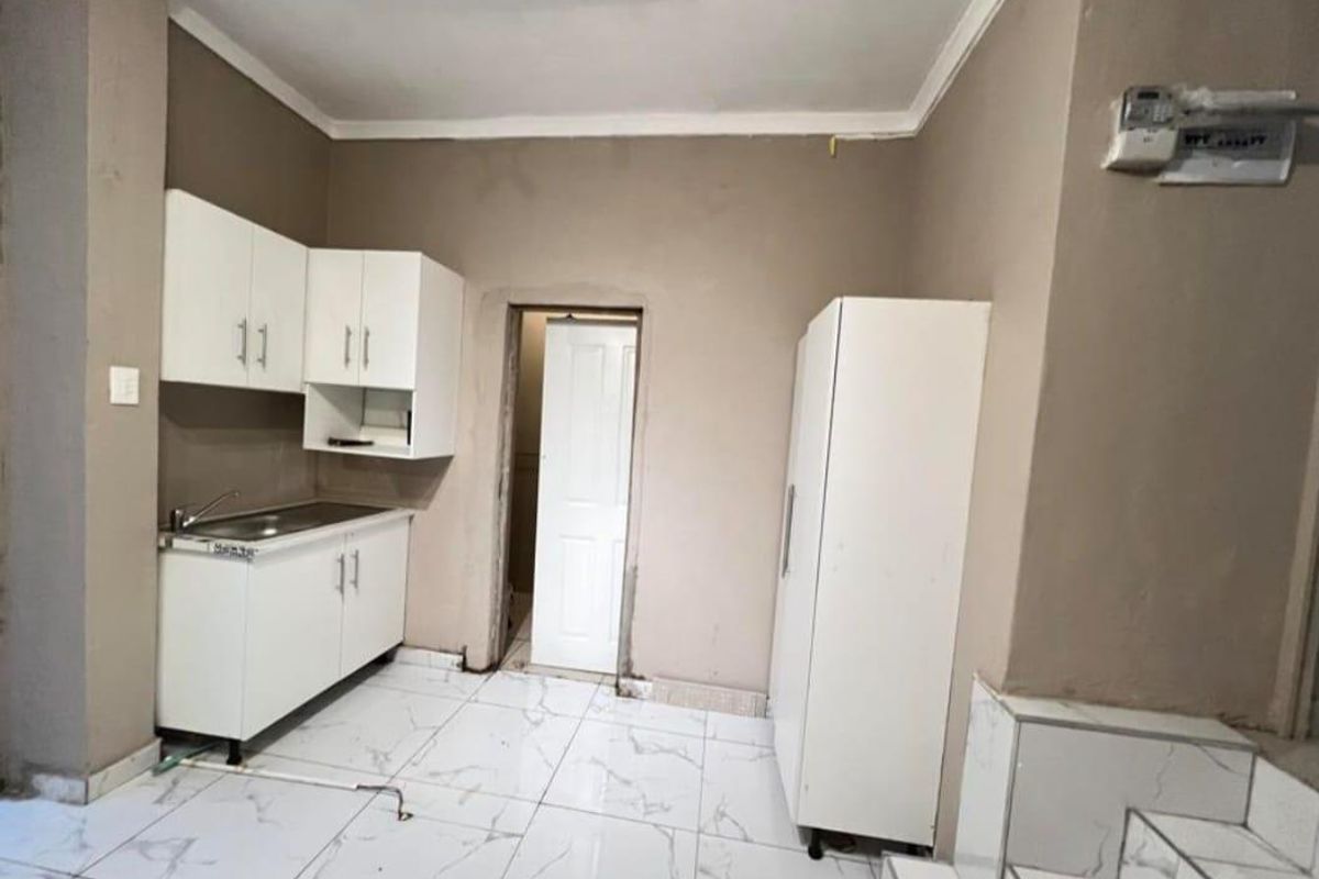 A compact kitchen area featuring white cabinetry, a stainless steel sink, and tiled flooring, requiring cosmetic updates and finishing touches.