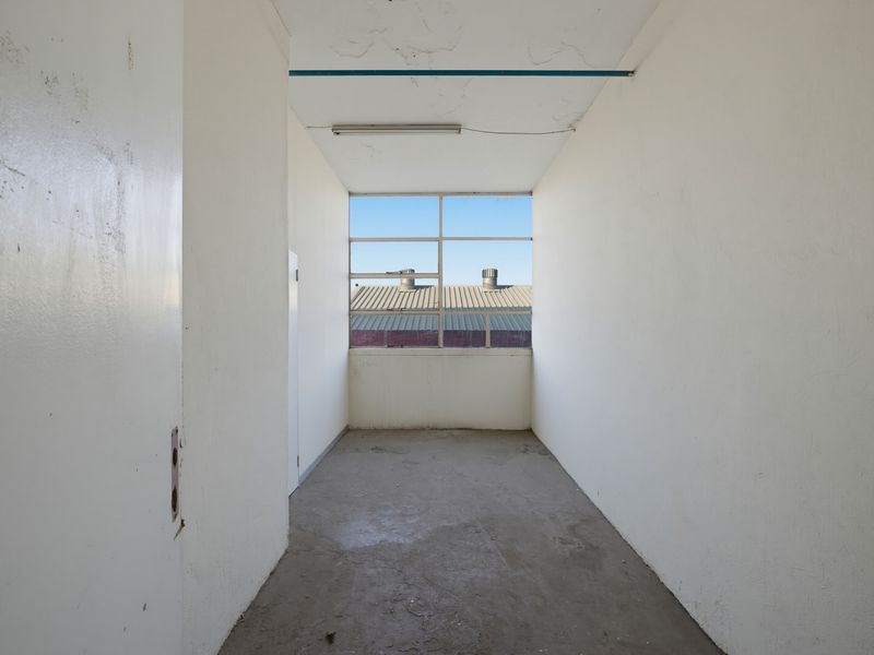 An empty utility space featuring a large metal-framed window, fluorescent lighting, and unfinished concrete flooring, suitable for storage or workshop use.