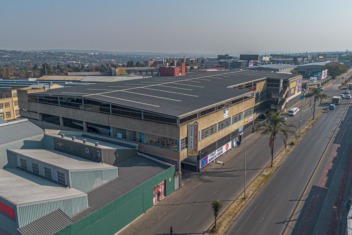 Aerial view of a multi-story industrial building featuring a large metal roof, concrete facade, and prominent street-level access in an established commercial area.