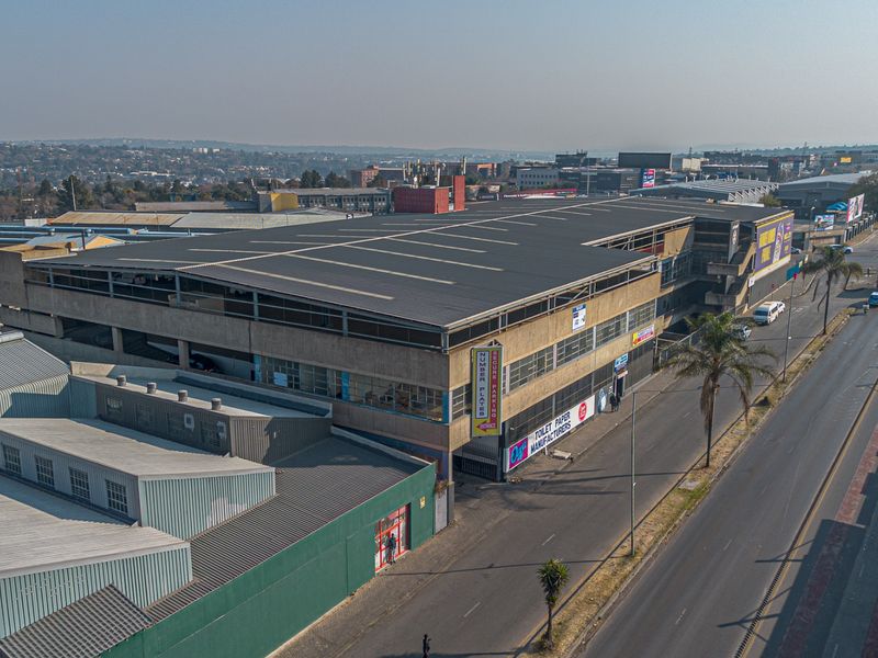 Aerial view of a multi-story industrial building featuring a large metal roof, concrete facade, and prominent street-level access in an established commercial area.