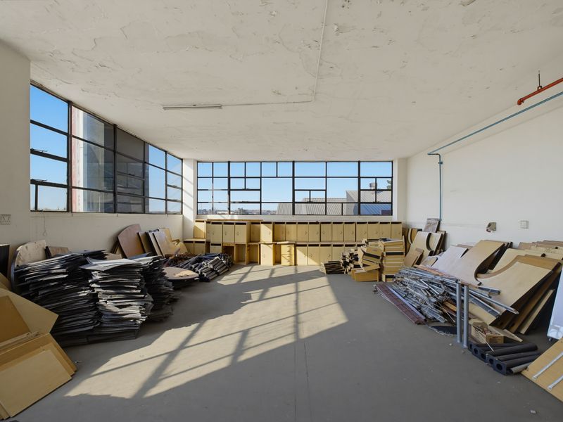 An open-plan industrial utility space featuring large steel-framed windows, exposed ceiling, and built-in storage lockers, currently used for storage.