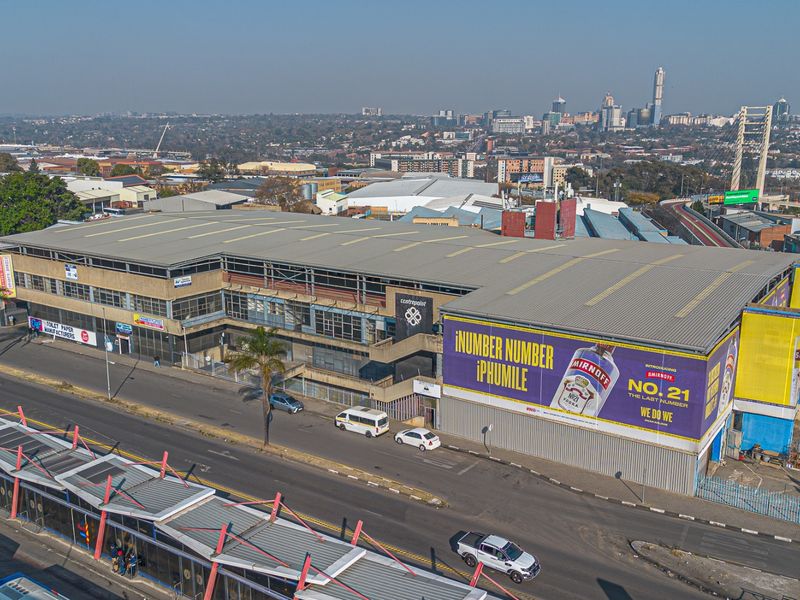 Aerial view of a large industrial warehouse facility featuring a metal roof, steel structure, and prominent exterior advertising signage in an urban setting.