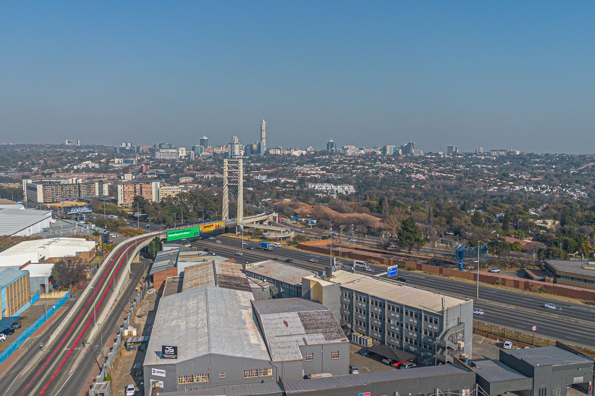 Aerial view of an industrial warehouse property situated adjacent to a major highway and bridge, showcasing the surrounding urban landscape.