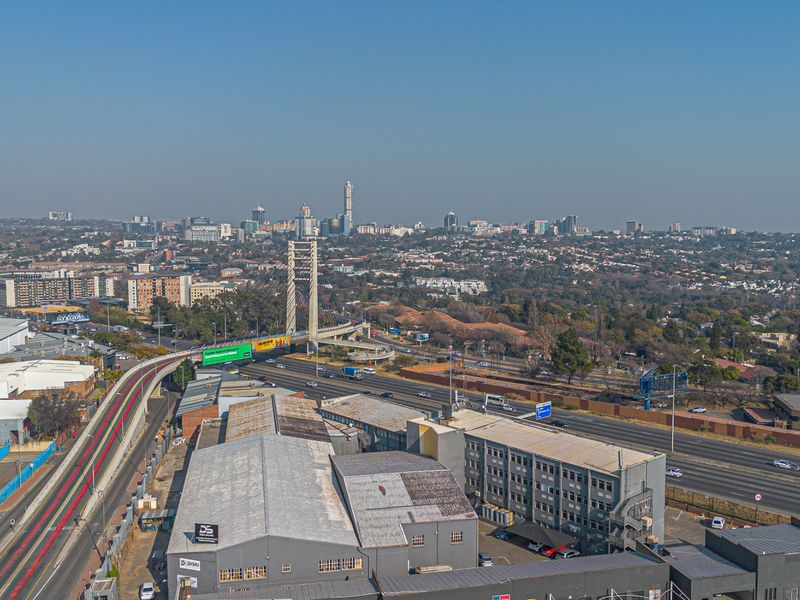 Aerial view of an industrial warehouse property situated adjacent to a major highway and bridge, showcasing the surrounding urban landscape.
