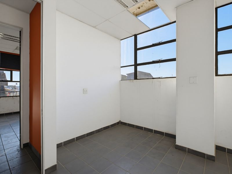 An empty office space featuring tiled flooring, large metal-framed windows, and a suspended ceiling, requiring minor maintenance and cosmetic updates.