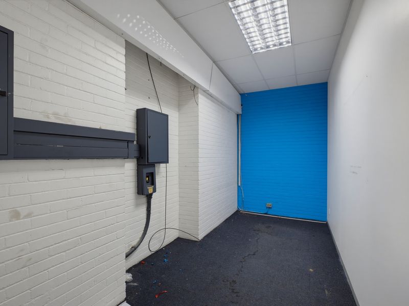A functional utility space featuring exposed brick walls, carpet flooring, and a mounted electrical distribution board, suitable for storage or technical use.