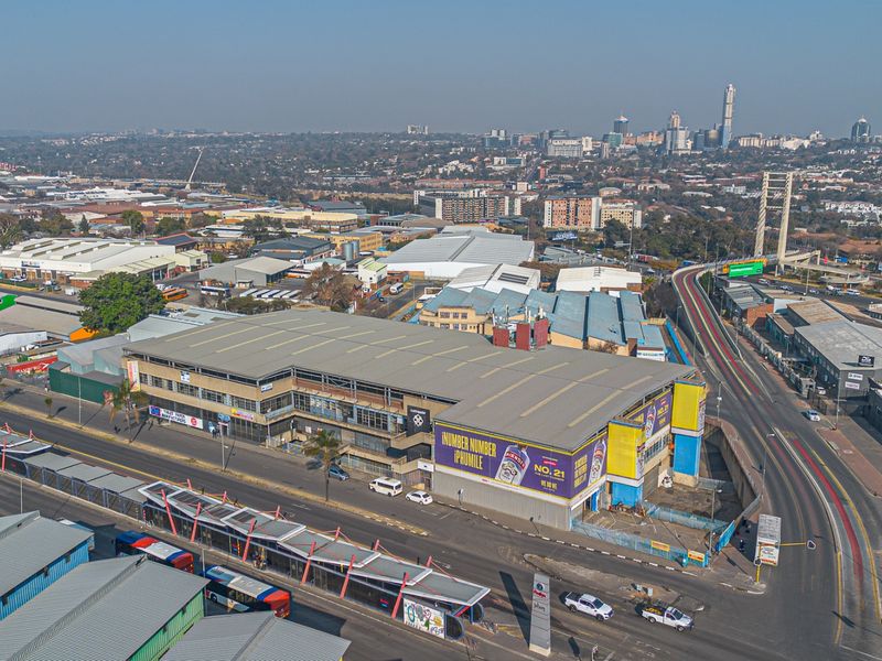 Aerial view of a large industrial warehouse facility situated in a commercial district, featuring prominent street frontage and proximity to major transport infrastructure.