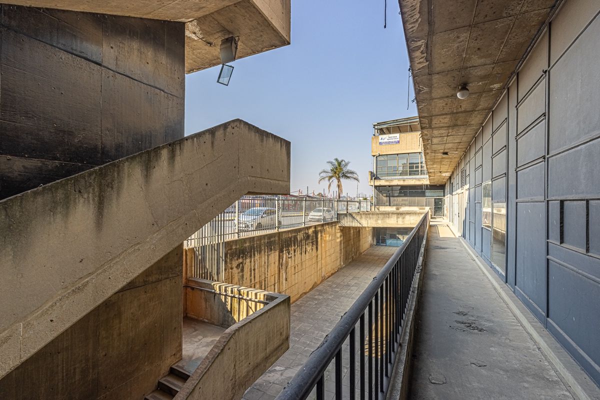 Exterior view of an industrial building featuring a concrete staircase, walkway, and metal security fencing with visible weathering on the concrete surfaces.