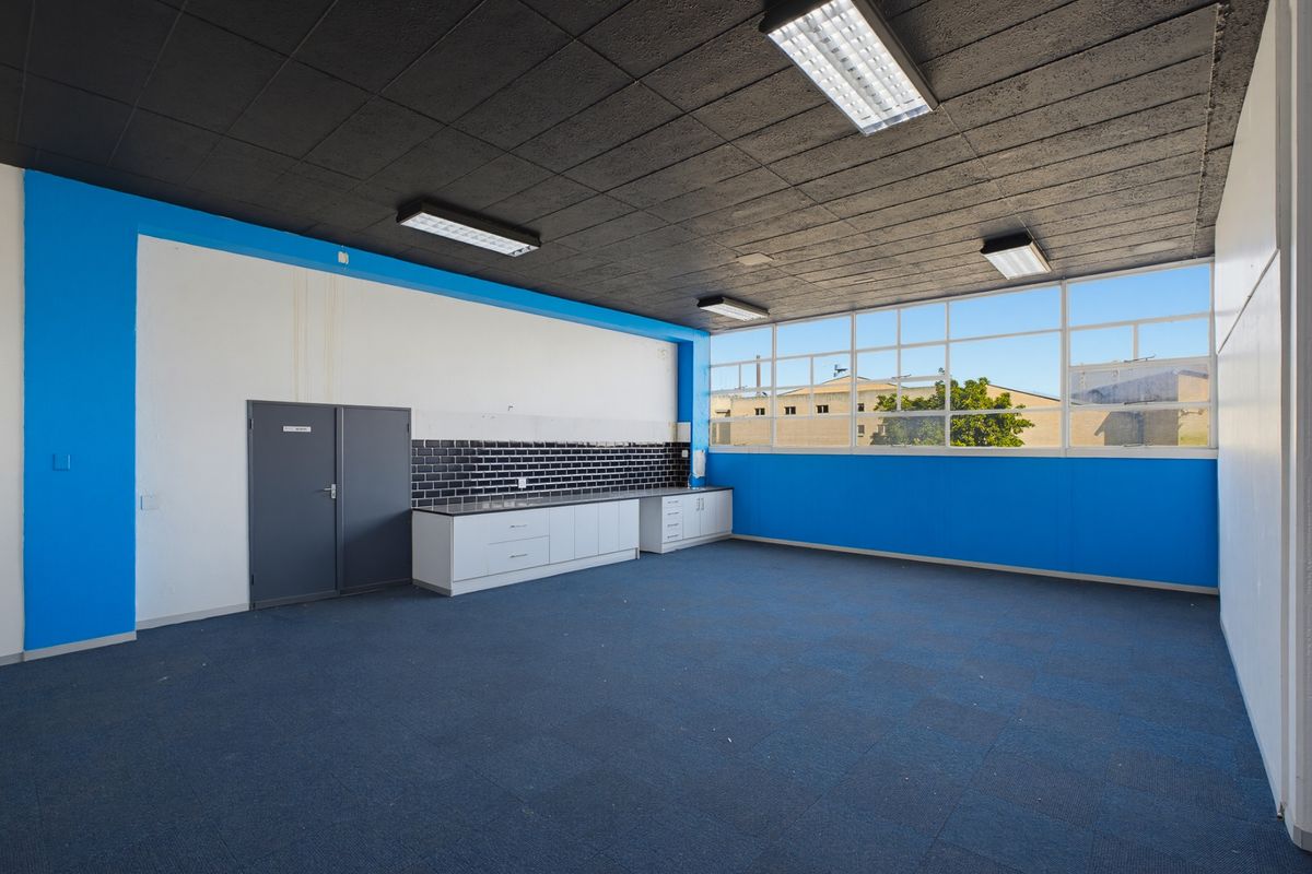 An empty industrial-style kitchen area featuring built-in cabinetry, a black tiled splashback, large windows, and fluorescent lighting.