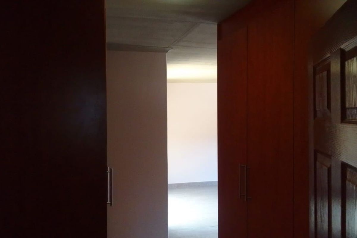 A view through a doorway into an empty bedroom featuring built-in wooden cupboards and a traditional panel door.