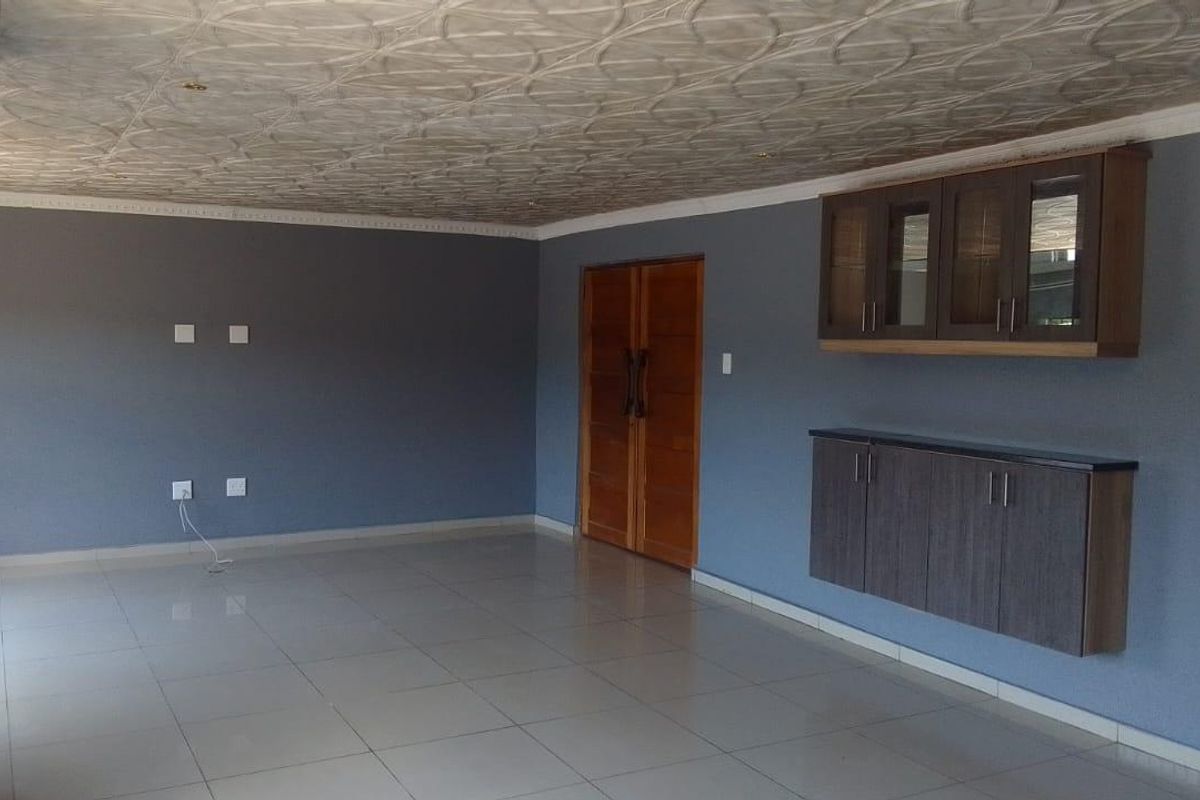 Spacious living area featuring tiled flooring, decorative ceiling tiles, and built-in wall-mounted cabinetry, providing a clean and versatile space.