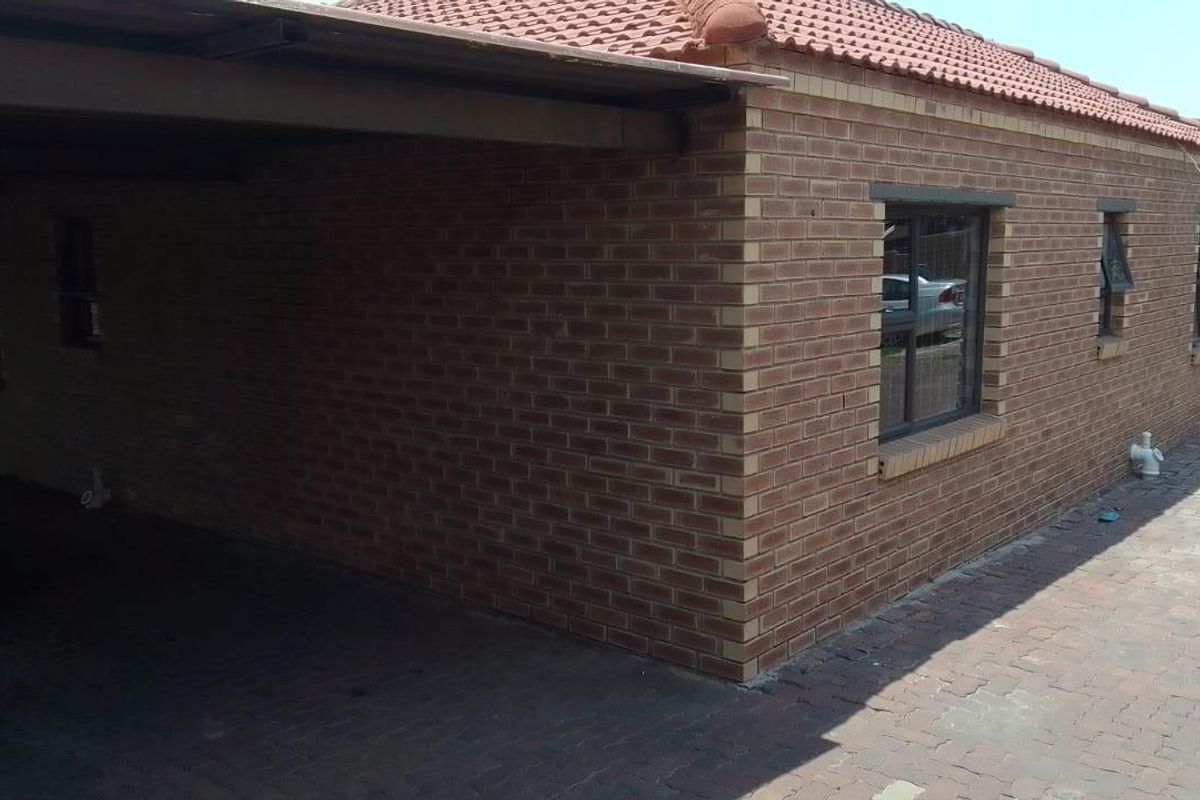 A view of the property's exterior featuring a face brick facade, tiled roof, and a covered carport area with paved driveway.